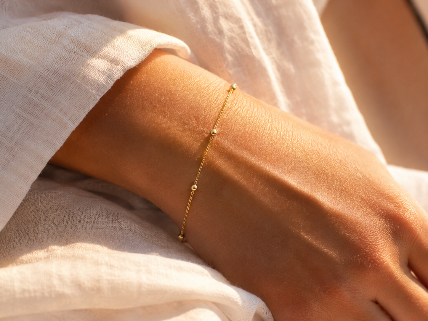 Bracelet chaîne boule en or jaune 18 carats avec petites boules de 1.8mm porté au poignet d'une femme au soleil.