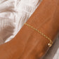 Gros plan sur le poignet d'une femme portant un bracelet en or jaune 14 carats orné d'une pampille en forme de cœur et d'une maille jaseron.