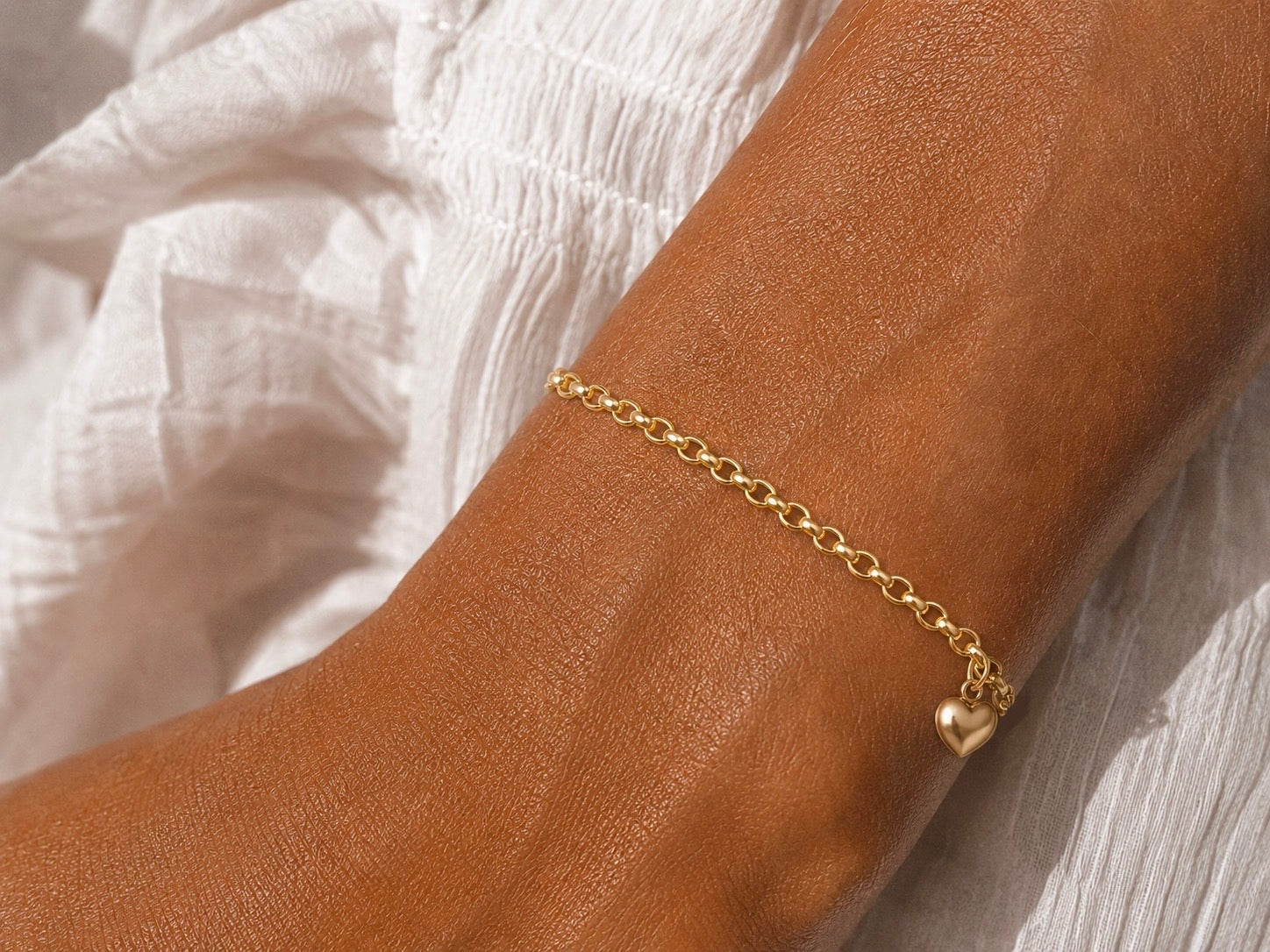 Gros plan sur le poignet d'une femme portant un bracelet en or jaune 14 carats orné d'une pampille en forme de cœur et d'une maille jaseron.