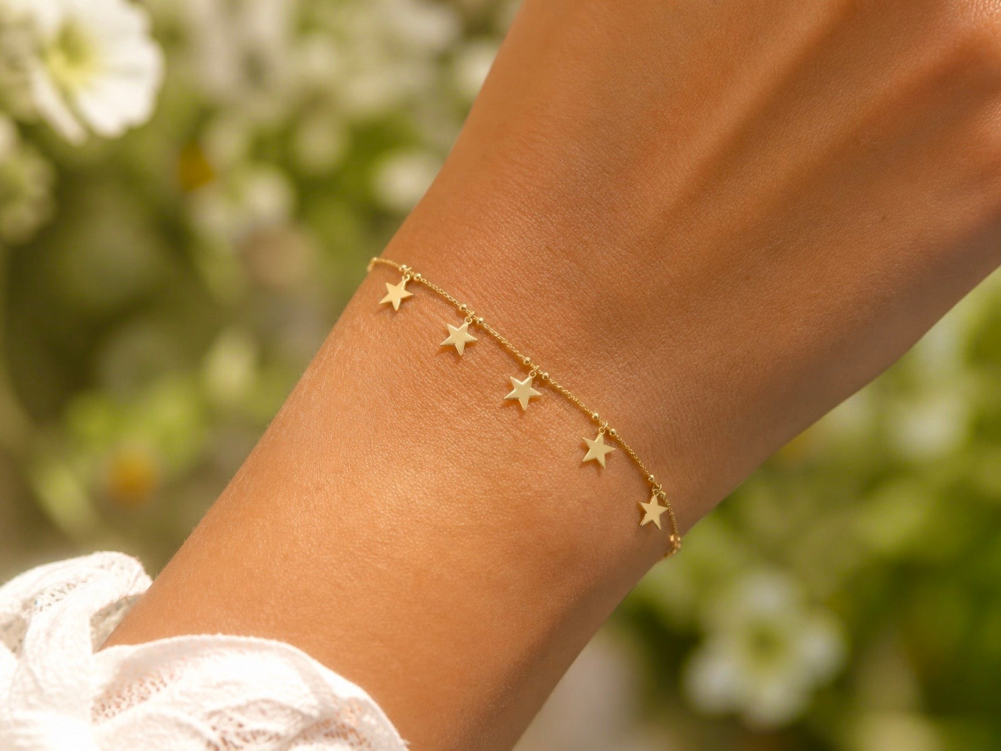 Gros plan sur le poignet d'une femme portant un bracelet étoile en or jaune 18 carats orné de 5 breloques pampilles, style bohème et solaire.