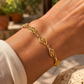 Gros plan sur le poignet d'une femme portant un bracelet en filigrane d'or jaune 18 carats, mettant en valeur le travail de dentelle d'or et les motifs ajourés.