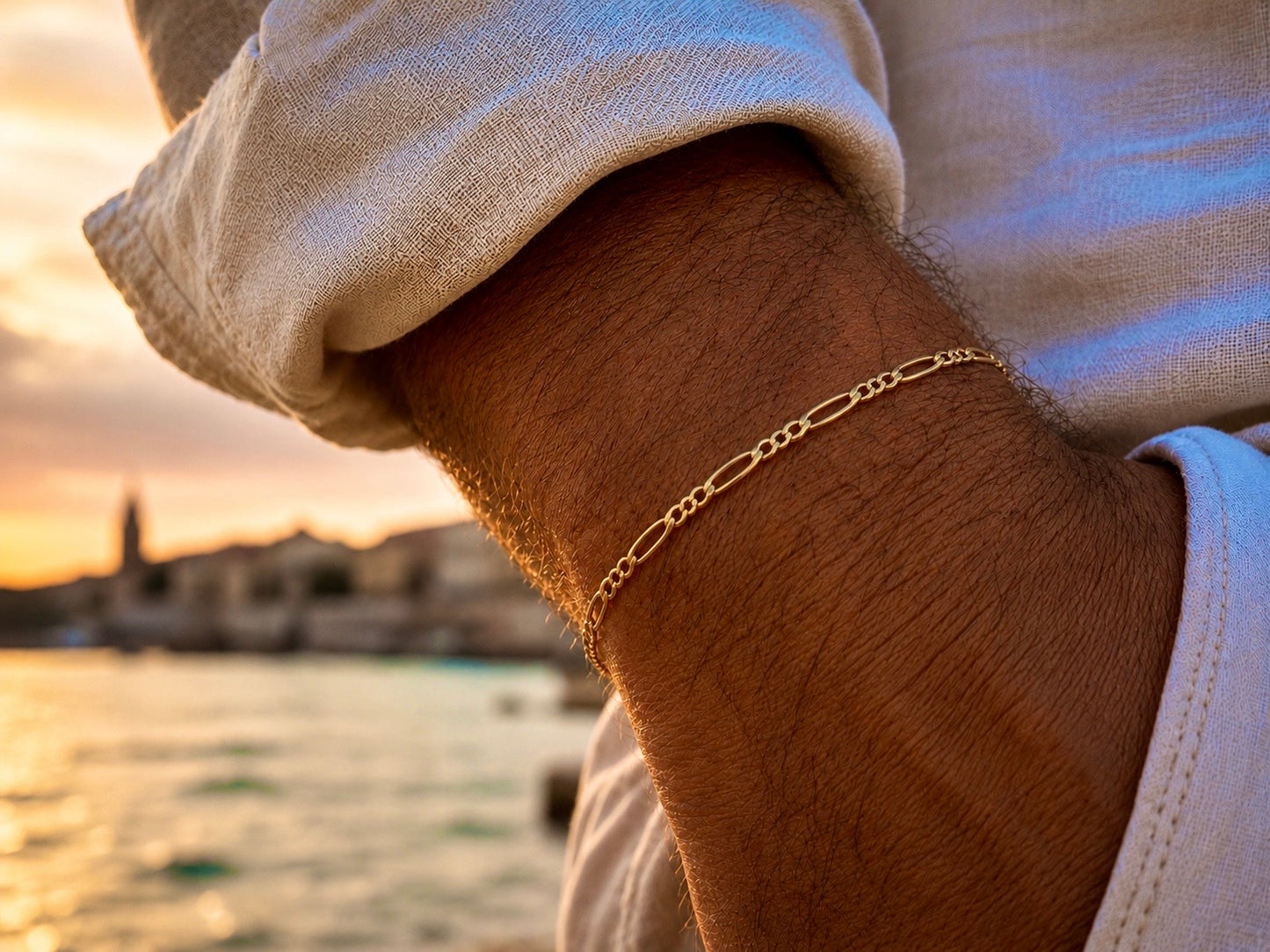 Gros plan sur un poignet d'homme portant un bracelet maille Figaro en or jaune 18 carats de 3 mm, style élégant et solaire.