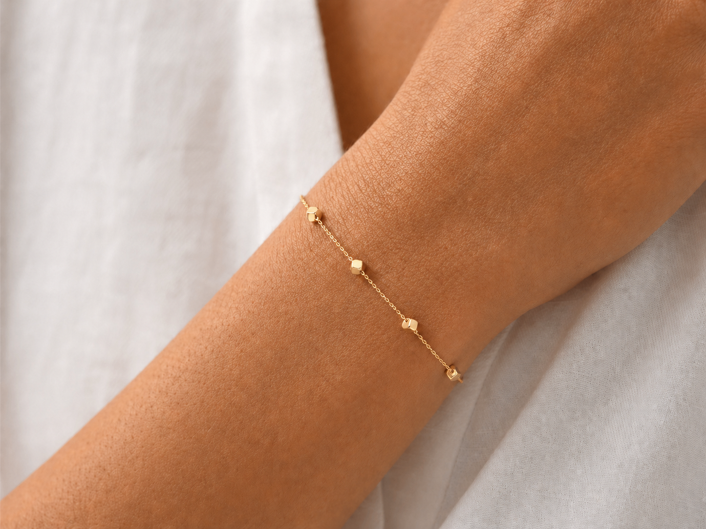 Gros plan sur un poignet de femme portant un bracelet fin en or jaune 18 carats orné de 8 petits cubes polis.