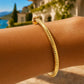 Gros plan sur le poignet d'une femme portant un bracelet jonc carré ciselé en or jaune 18 carats, éclat solaire et design géométrique.