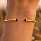 Poignet fin portant un bracelet jonc ouvert en or jaune 18 carats serti de deux rubis naturels, un bijou élégant conçu pour ne pas tourner.