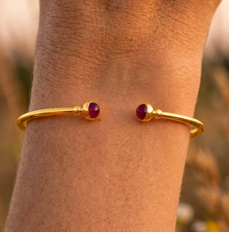 Poignet fin portant un bracelet jonc ouvert en or jaune 18 carats serti de deux rubis naturels, un bijou élégant conçu pour ne pas tourner.