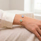 Gros plan sur le poignet d'une femme portant un bracelet jonc en or jaune 18 carats orné d'une aigue-marine et d'une aventurine de forme carrée.