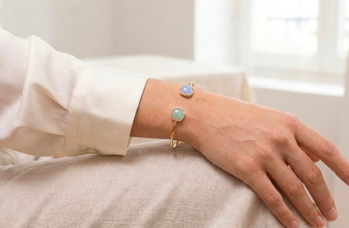 Gros plan sur le poignet d'une femme portant un bracelet jonc en or jaune 18 carats orné d'une aigue-marine et d'une aventurine de forme carrée.