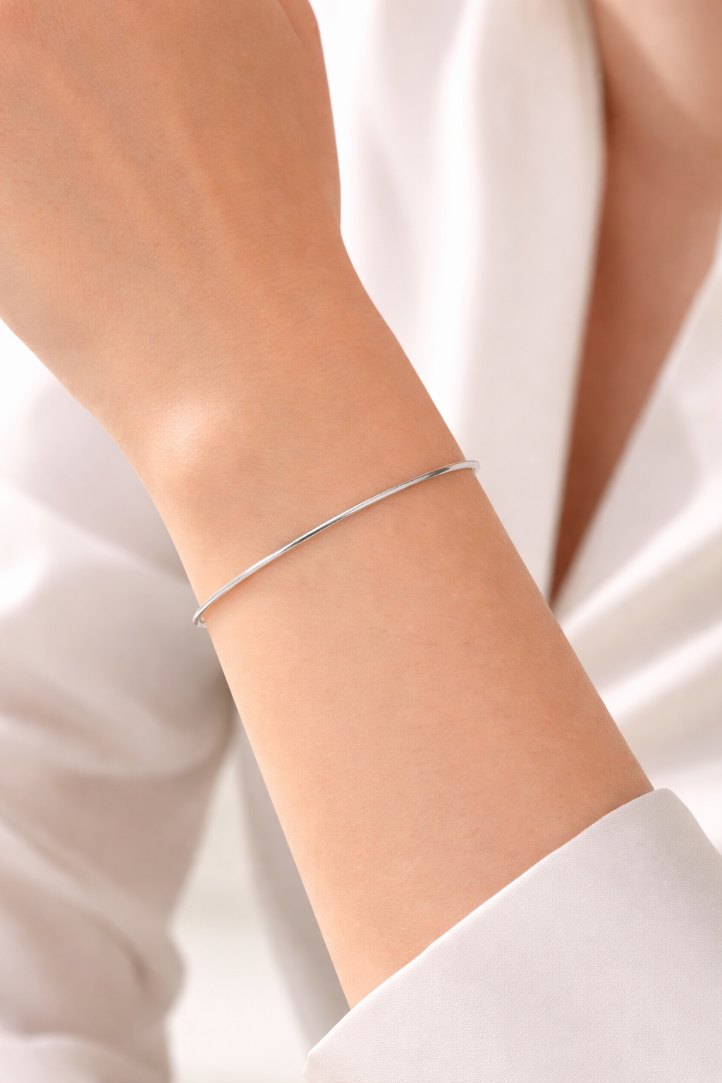 Gros plan sur un poignet de femme portant un bracelet jonc or blanc 18 carats. Jonc rond massif de 1,5mm en or blanc non rhodié.