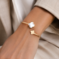 Bracelet jonc ouvert croisé en or jaune 18 carats avec trèfle en nacre blanche porté au poignet d'une femme élégante quiet luxury