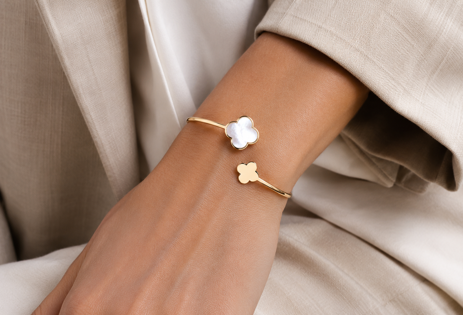Bracelet jonc ouvert croisé en or jaune 18 carats avec trèfle en nacre blanche porté au poignet d'une femme élégante quiet luxury