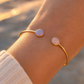 Bracelet jonc ouvert en or jaune 18 carats avec pierres naturelles opale et améthyste porté au poignet au soleil.
