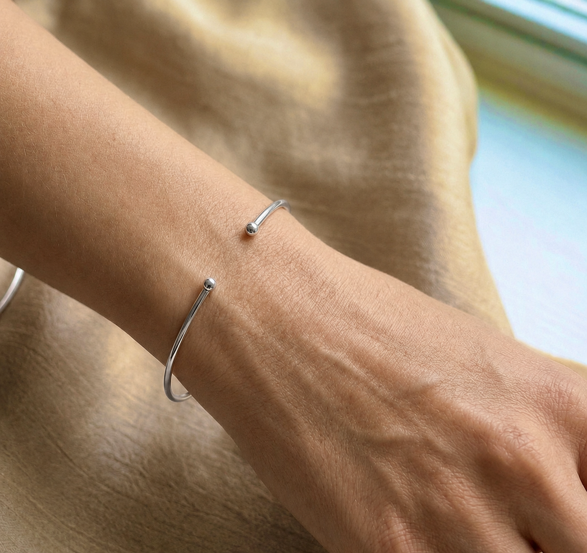 Poignet d'une femme portant un bracelet jonc ouvert en or blanc massif 18 carats, fil rond de 1,5 mm avec finitions boules.