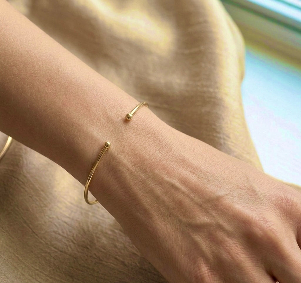 Gros plan sur le poignet d'une femme portant un bracelet jonc ouvert en or jaune massif 18 carats, fil rond de 1,5 mm avec finitions boules.