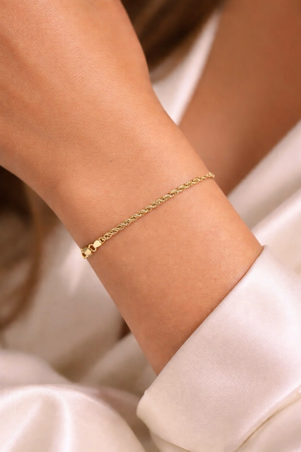 Gros plan sur un poignet de femme portant un bracelet maille corde en or jaune 18 carats au design torsadé.