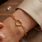 Bracelet trombone en or jaune 18 carats avec fermoir en forme de coeur porté au poignet d'une femme.