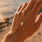 Gros plan sur la gestuelle d'une femme portant une chaîne de main en or 18 carats avec fleur et perles en résine blanche.