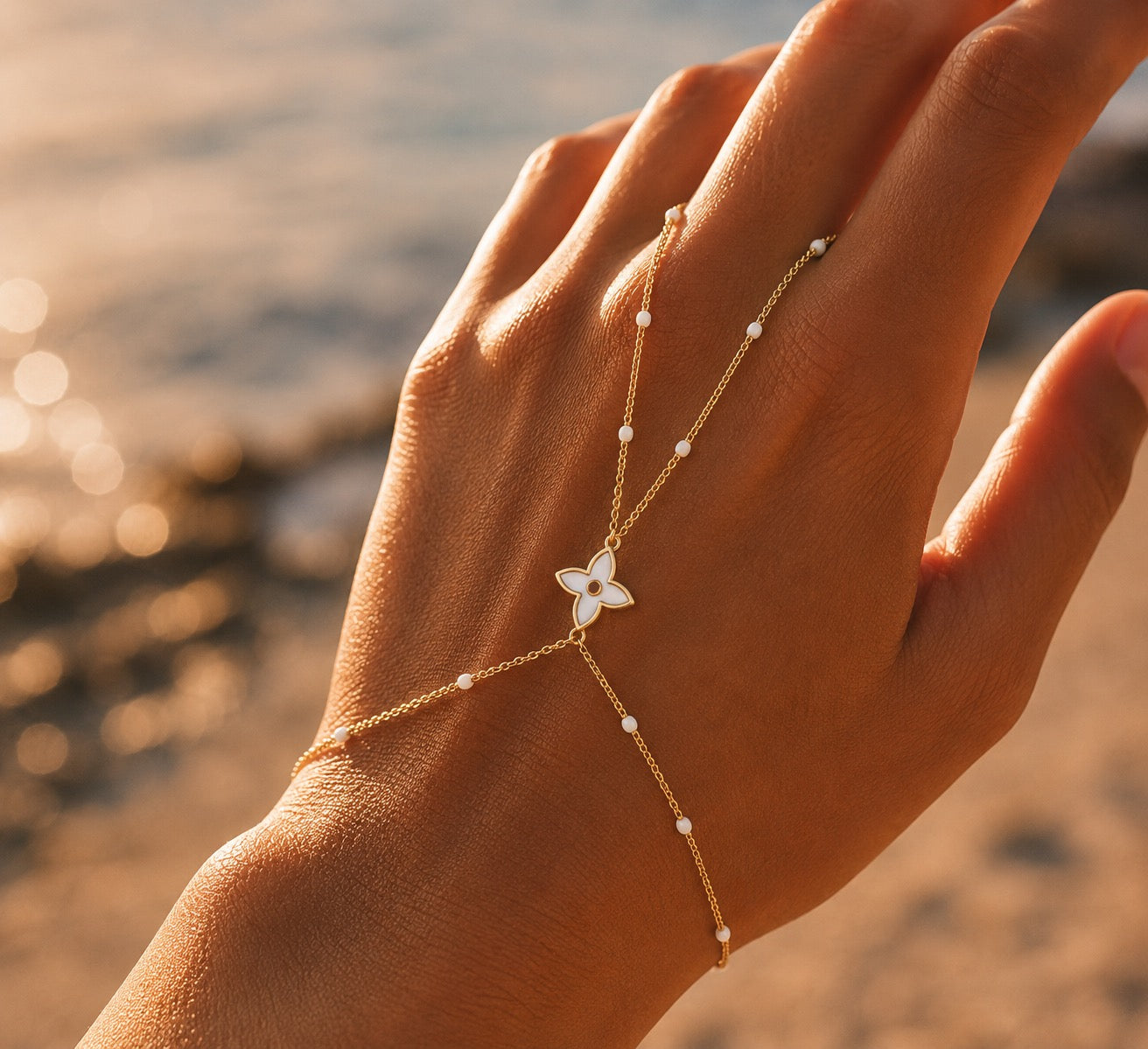 Gros plan sur la gestuelle d'une femme portant une chaîne de main en or 18 carats avec fleur et perles en résine blanche.