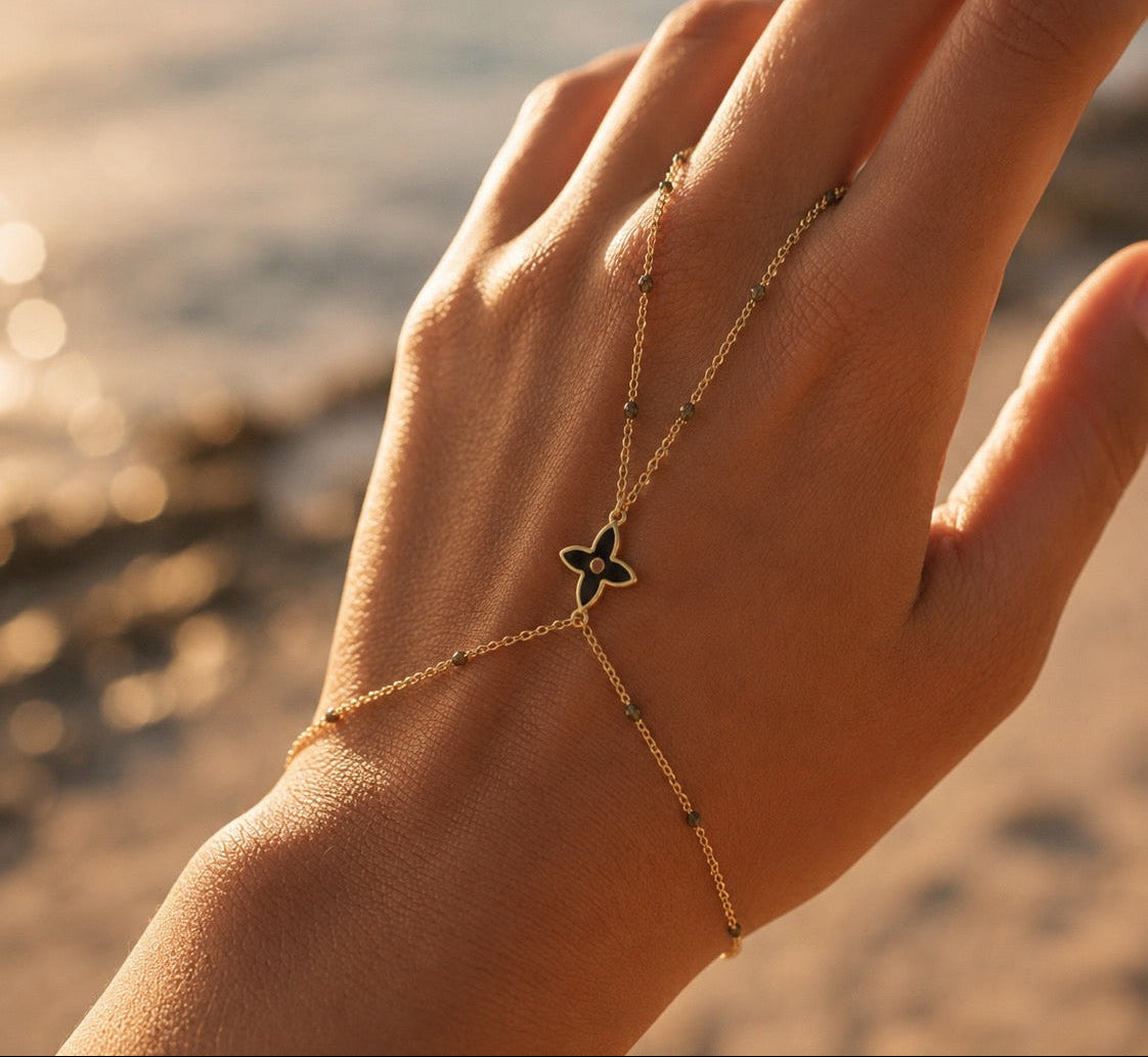 Gros plan sur une main de femme portant une chaîne de main en or jaune 18 carats avec motif fleur et perles en résine noire.