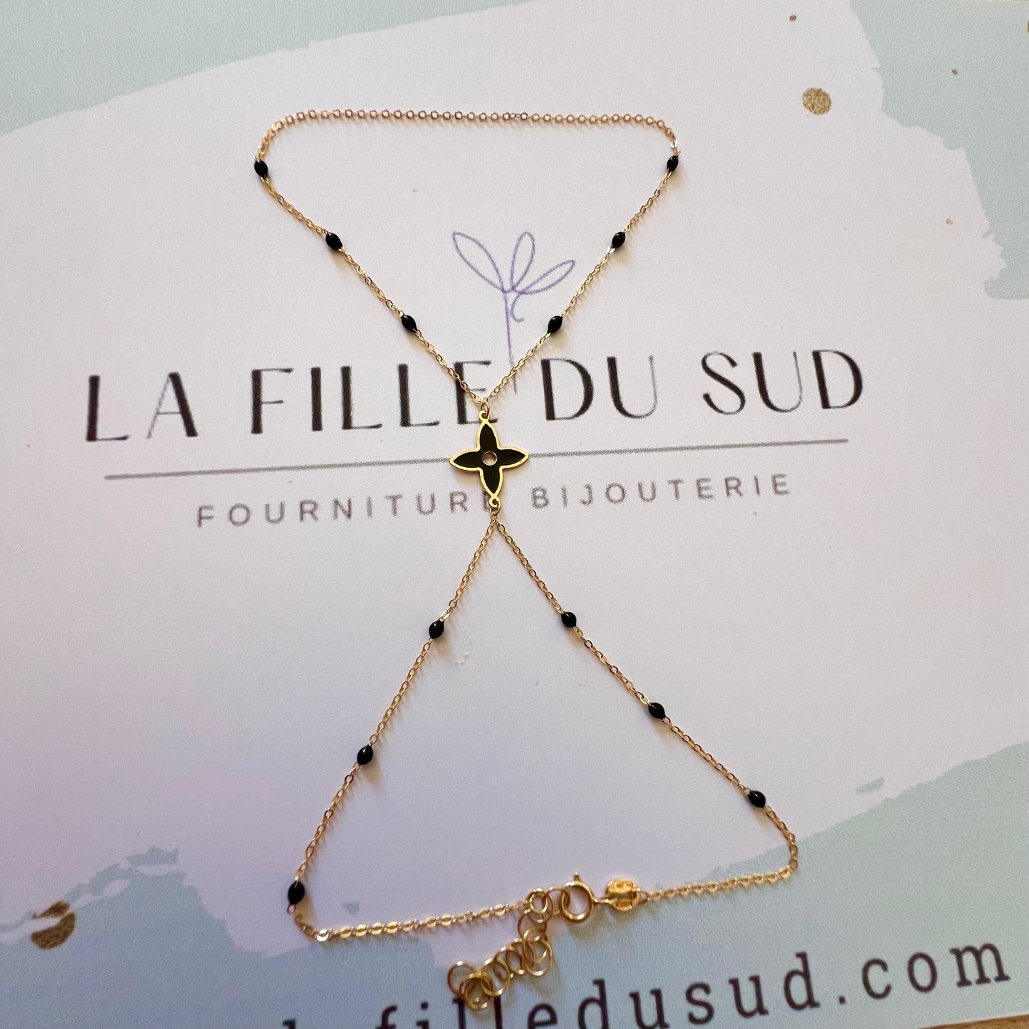 Chaîne de main en or jaune 18 carats avec motif fleur et perles en résine noire.