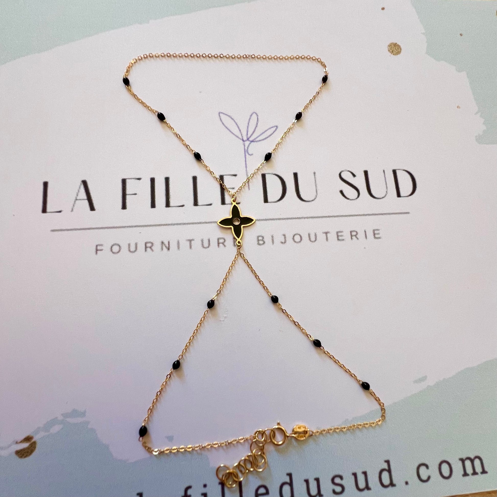 Chaîne de main en or jaune 18 carats avec motif fleur et perles en résine noire.