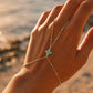 Main de femme ornée d'un bracelet de main en or 18 carats avec fleur et perles en résine turquoise, style bohème-chic.