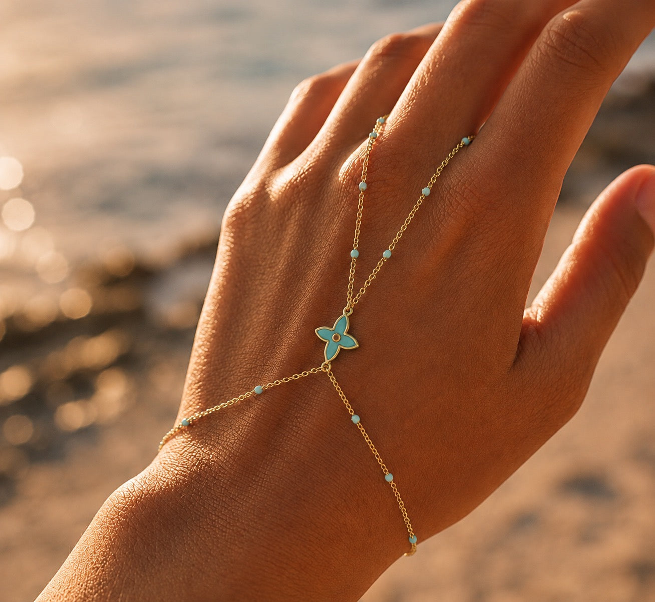 Main de femme ornée d'un bracelet de main en or 18 carats avec fleur et perles en résine turquoise, style bohème-chic.