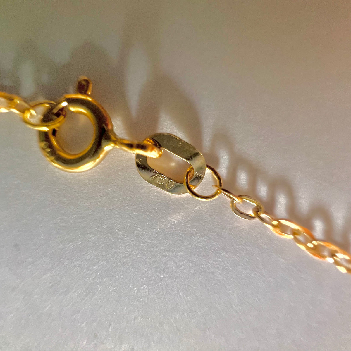 Gros plan du poinçon officiel 750 garantissant l'or jaune 18 carats sur l'attache du fermoir ressort de la chaîne homme.