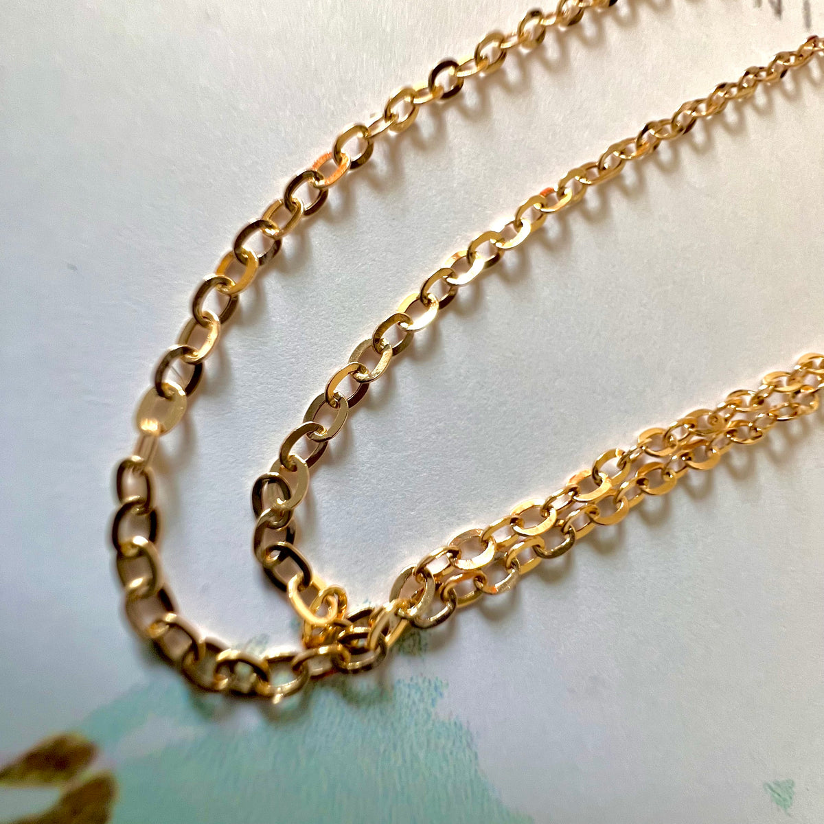 Chaîne en or jaune 18 carats maille forçat miroir captant la lumière naturelle du soleil.