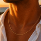 Gros plan sur un homme portant une chaîne maille forçat miroir en or jaune 18 carats de 50 cm, un collier masculin élégant et brillant.