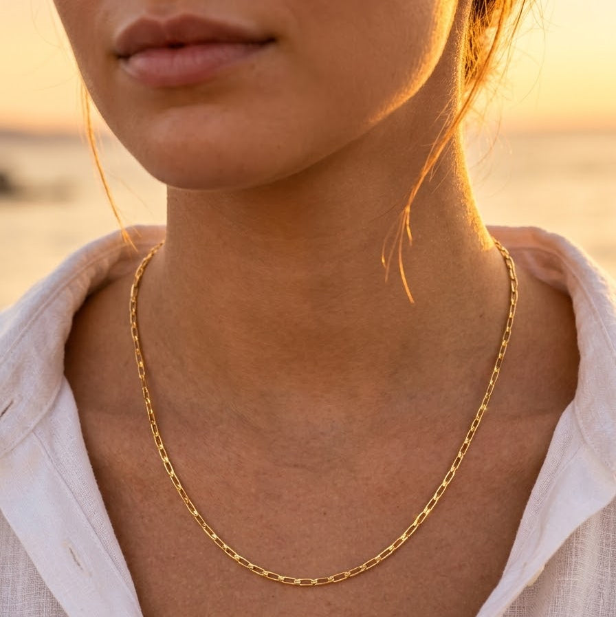 Collier chaîne maille cheval en or jaune 18 carats porté avec élégance par une femme au coucher du soleil.
