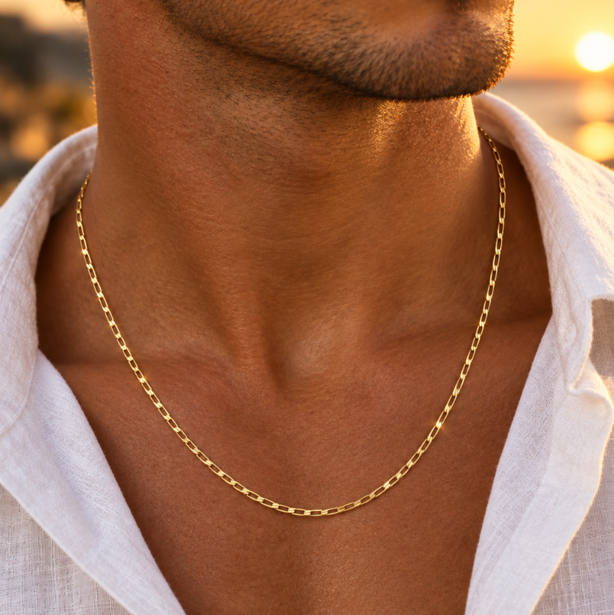 Chaîne en or massif 18 carats maille cheval portée sur le torse d'un homme en chemise de lin sous une lumière solaire.