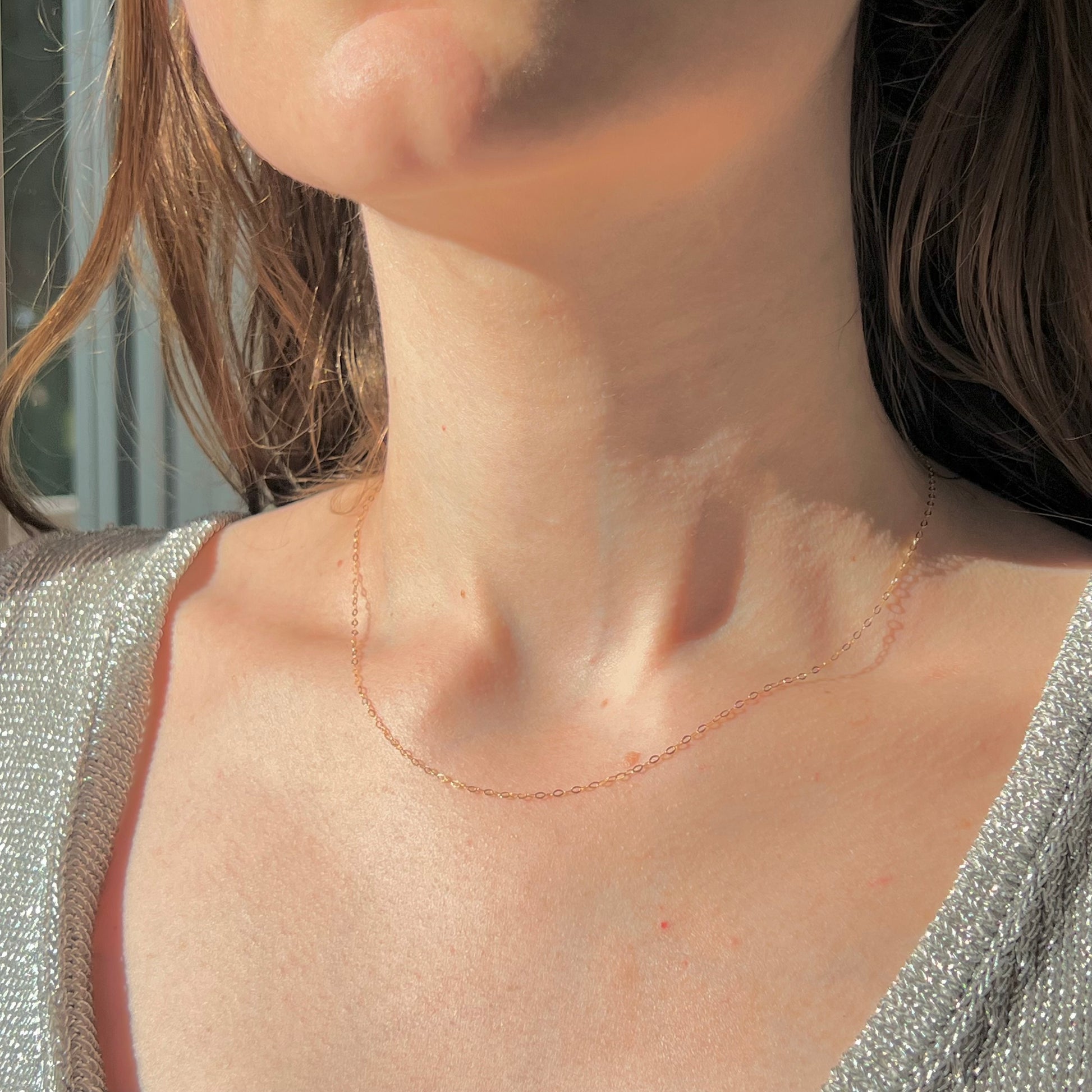 Femme portant une chaînette fine en or 18 carats au creux du cou, longueur standard 42 cm.
