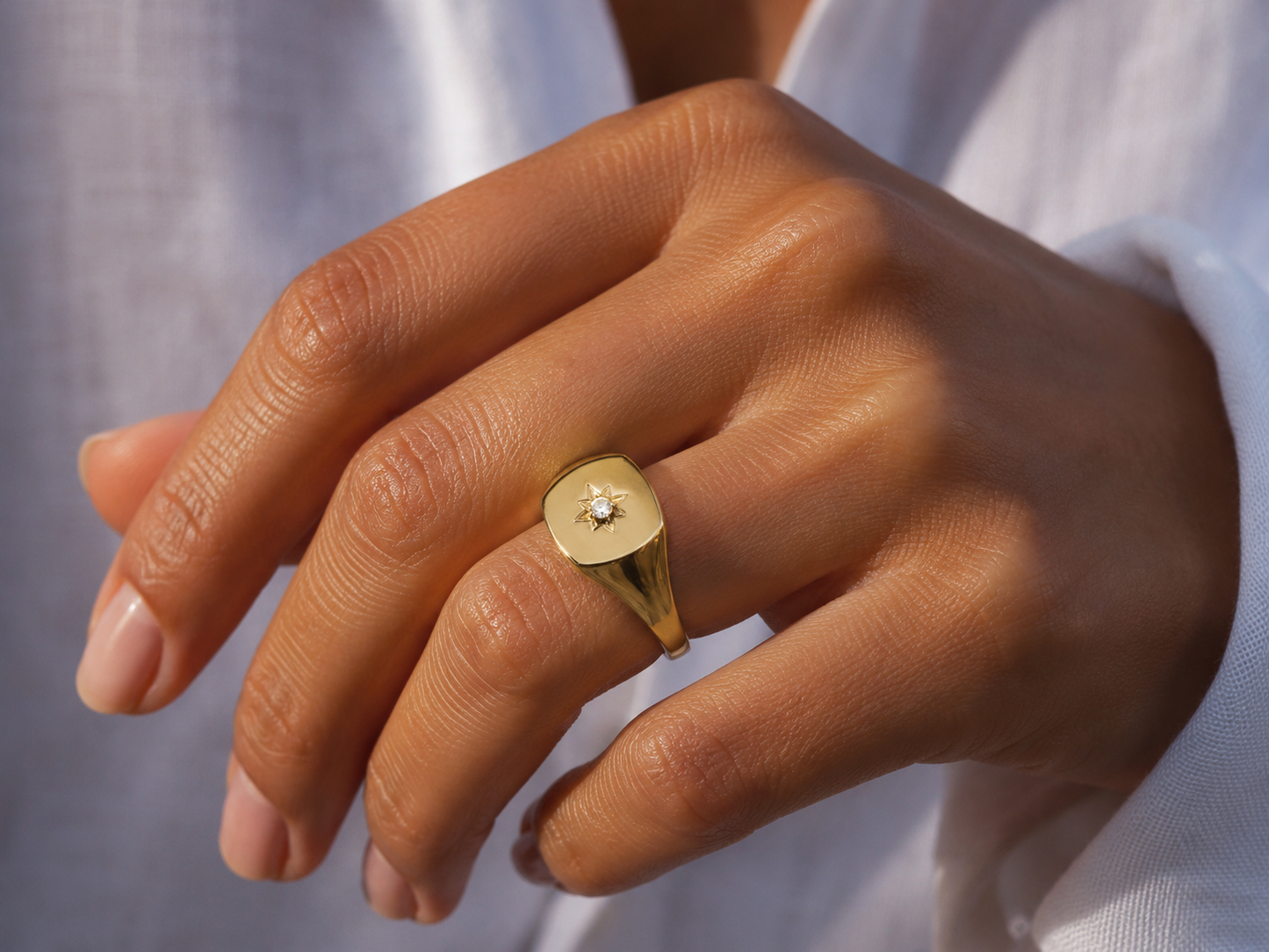 Gros plan sur une main de femme portant une chevalière en or jaune 18 carats ornée d'une étoile du Nord et d'un diamant étincelant.