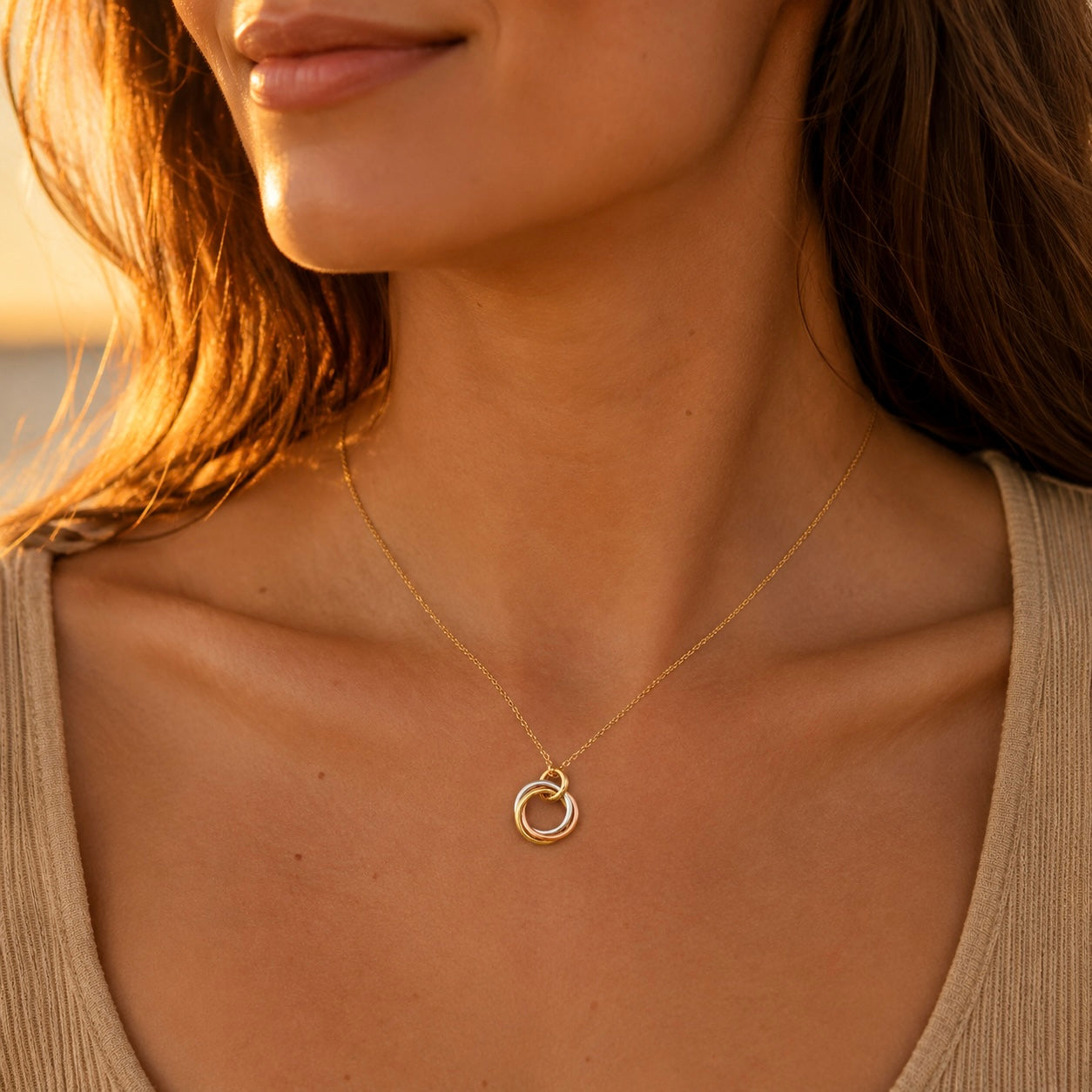 Collier 3 anneaux entrelacés en or jaune 18 carats massif porté par une femme de profil au coucher du soleil.