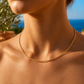 Gros plan sur le décolleté d'une femme portant un collier câble en or jaune 18 carats massif, une chaîne rigide de 1,4 mm au design minimaliste.