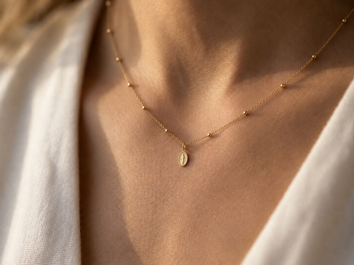 Collier catholique Vierge Marie en or jaune 18 carats porté au creux du cou d'une femme au coucher du soleil.