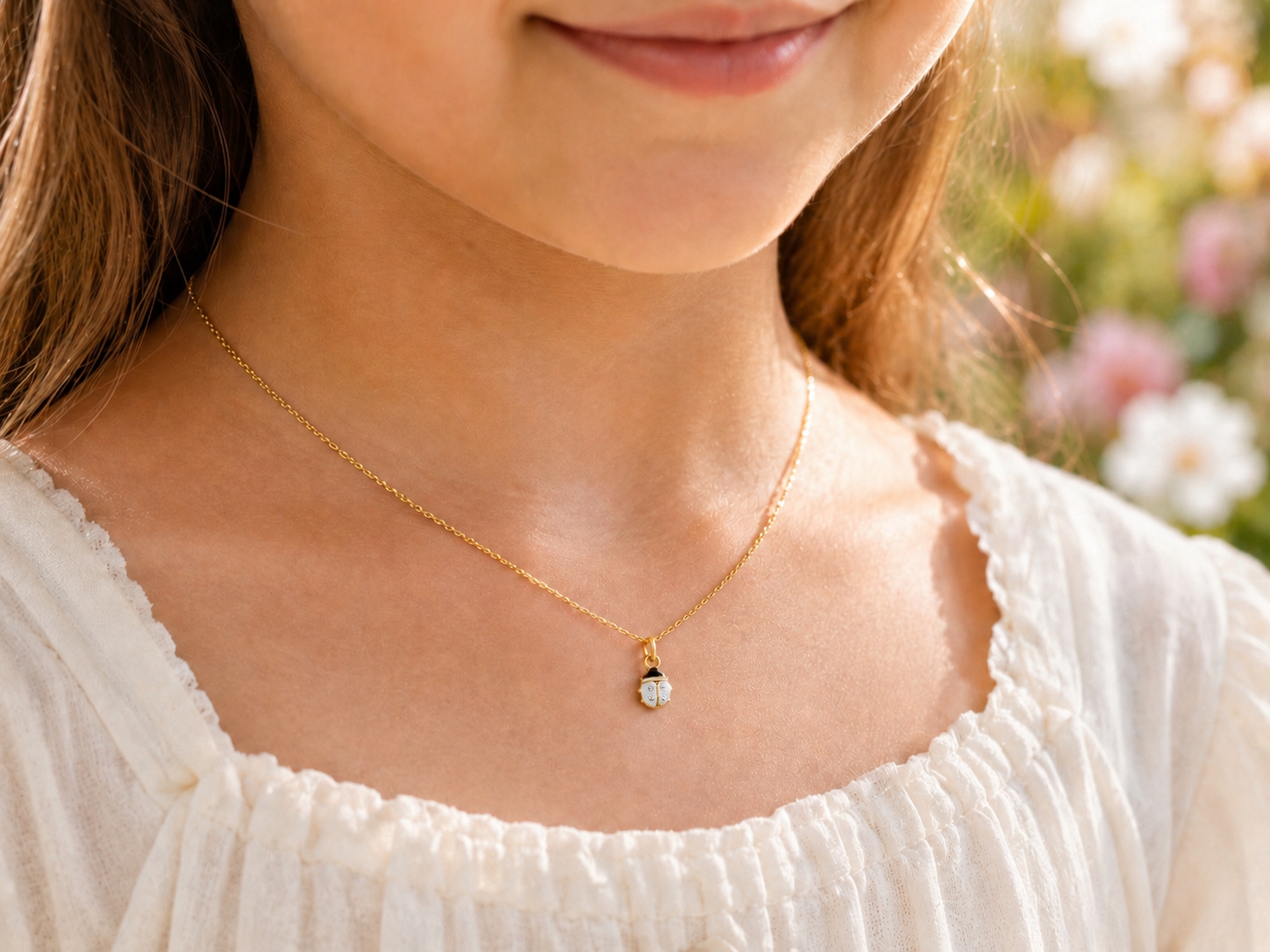 Décolleté d'une fillette portant un collier coccinelle blanche en or jaune 18 carats, un bijou de baptême pur et élégant.