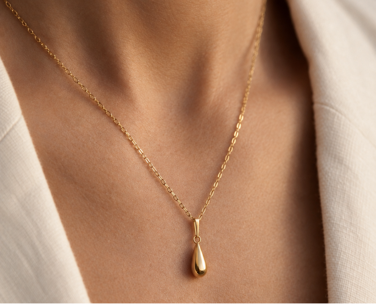 Pendentif goutte d'eau en or jaune 18 carats porté sur une chaîne forçat miroir au coucher du soleil.