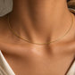 Gros plan sur le décolleté d'une femme portant un collier maille Oméga en or jaune 18 carats, une chaîne ronde de 1 mm au design lisse et élégant.