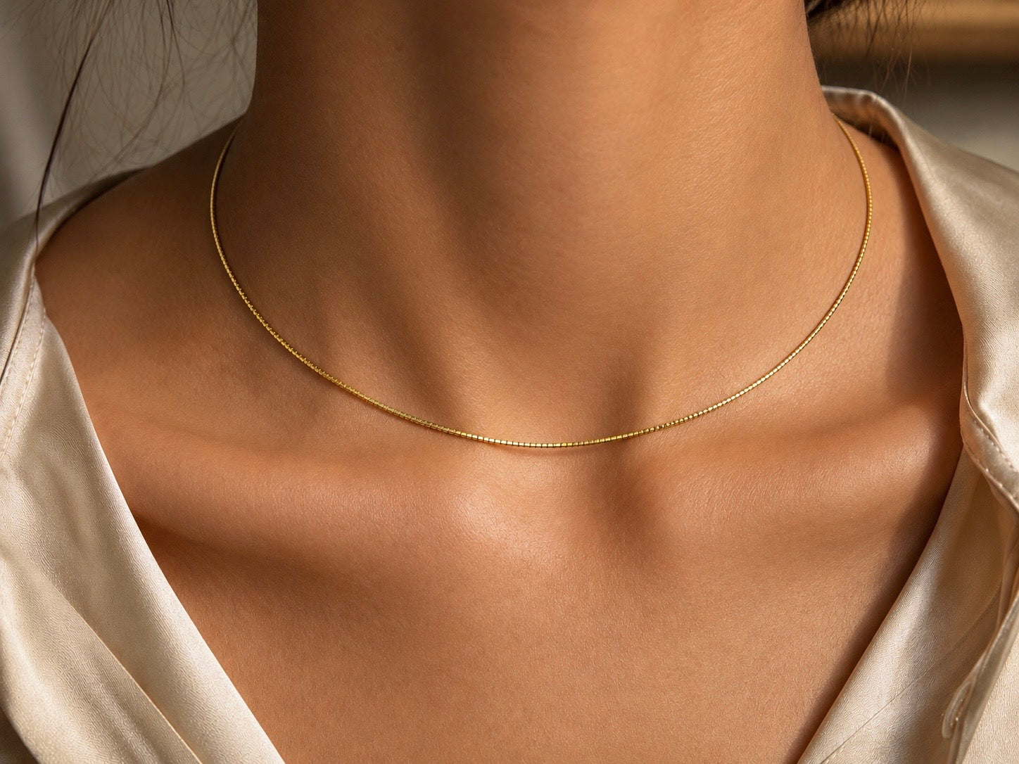 Gros plan sur le décolleté d'une femme portant un collier maille Oméga en or jaune 18 carats, une chaîne ronde de 1 mm au design lisse et élégant.