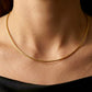 Gros plan sur une femme portant le collier maille Oméga en or jaune 18 carats de 42 cm, un porté princesse élégant qui souligne la base du cou.