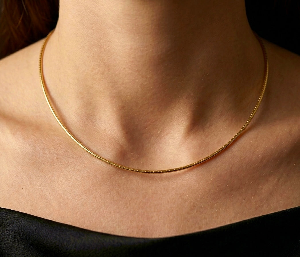 Gros plan sur une femme portant le collier maille Oméga en or jaune 18 carats de 42 cm, un porté princesse élégant qui souligne la base du cou.