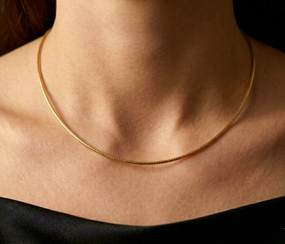 Gros plan sur une femme portant le collier maille Oméga en or jaune 18 carats de 42 cm, un porté princesse élégant qui souligne la base du cou.