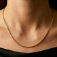Décolleté d'une femme portant le collier maille Oméga en or jaune 18 carats de 45 cm, mettant en valeur l'éclat miroir de la chaîne de 1,4 mm.