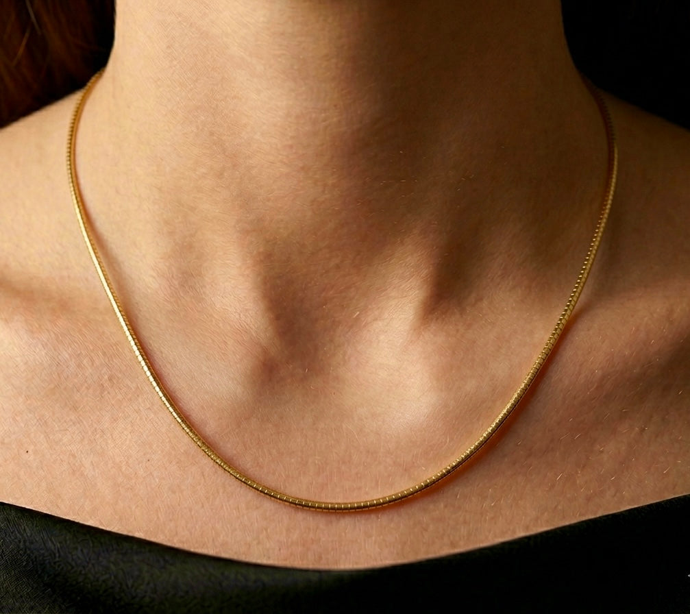 Décolleté d'une femme portant le collier maille Oméga en or jaune 18 carats de 45 cm, mettant en valeur l'éclat miroir de la chaîne de 1,4 mm.