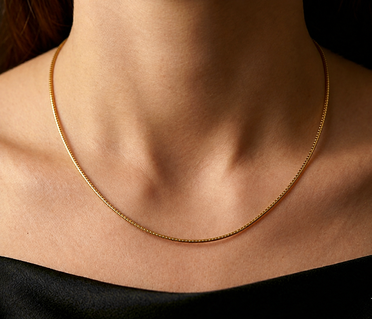 Décolleté d'une femme portant le collier maille Oméga en or jaune 18 carats de 45 cm, mettant en valeur l'éclat miroir de la chaîne de 1,4 mm.