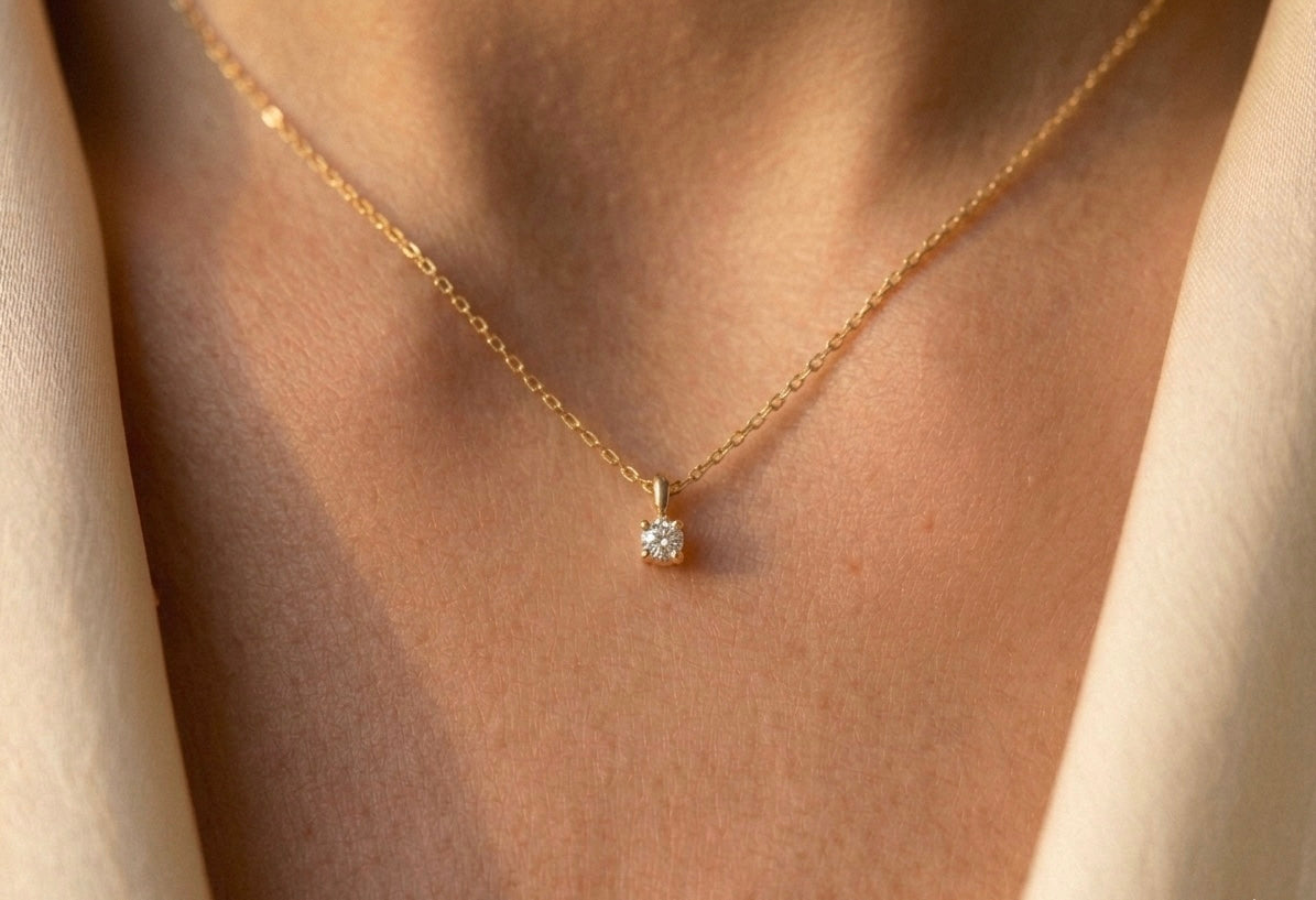 Gros plan sur le décolleté d'une femme portant un collier solitaire en or jaune 18 carats serti d'un diamant naturel de 0,15 carat.