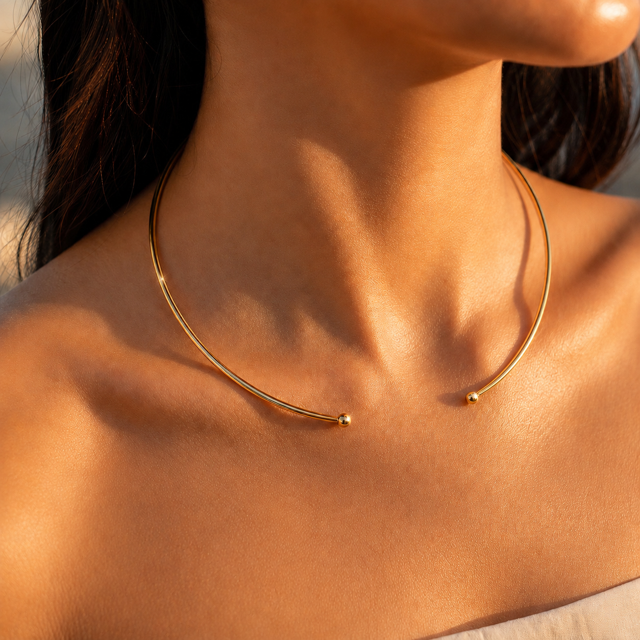 Collier jonc rigide ouvert en or jaune 18 carats posé sur les clavicules d'une femme au coucher du soleil.
