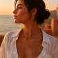 Collier torque rigide en or jaune 18 carats porté ouvert devant par une femme de profil habillée en blanc au crépuscule.